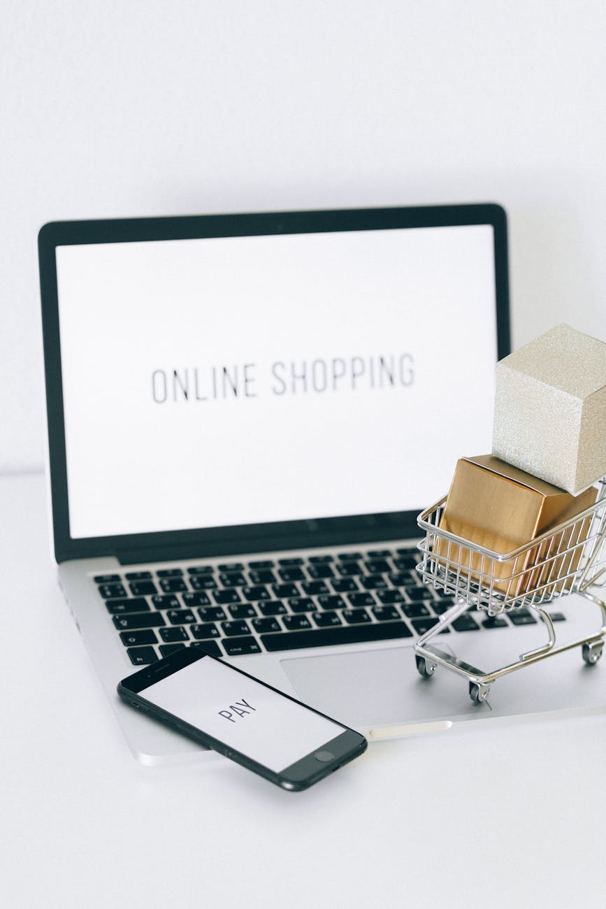 a miniature shopping cart and smartphone on macbook laptop